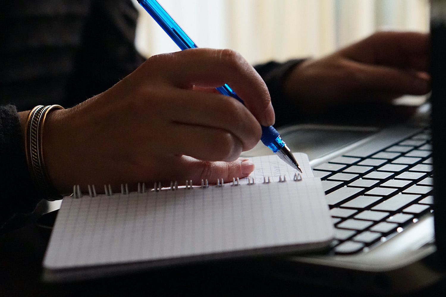 A person writing in a notebook while on their laptop