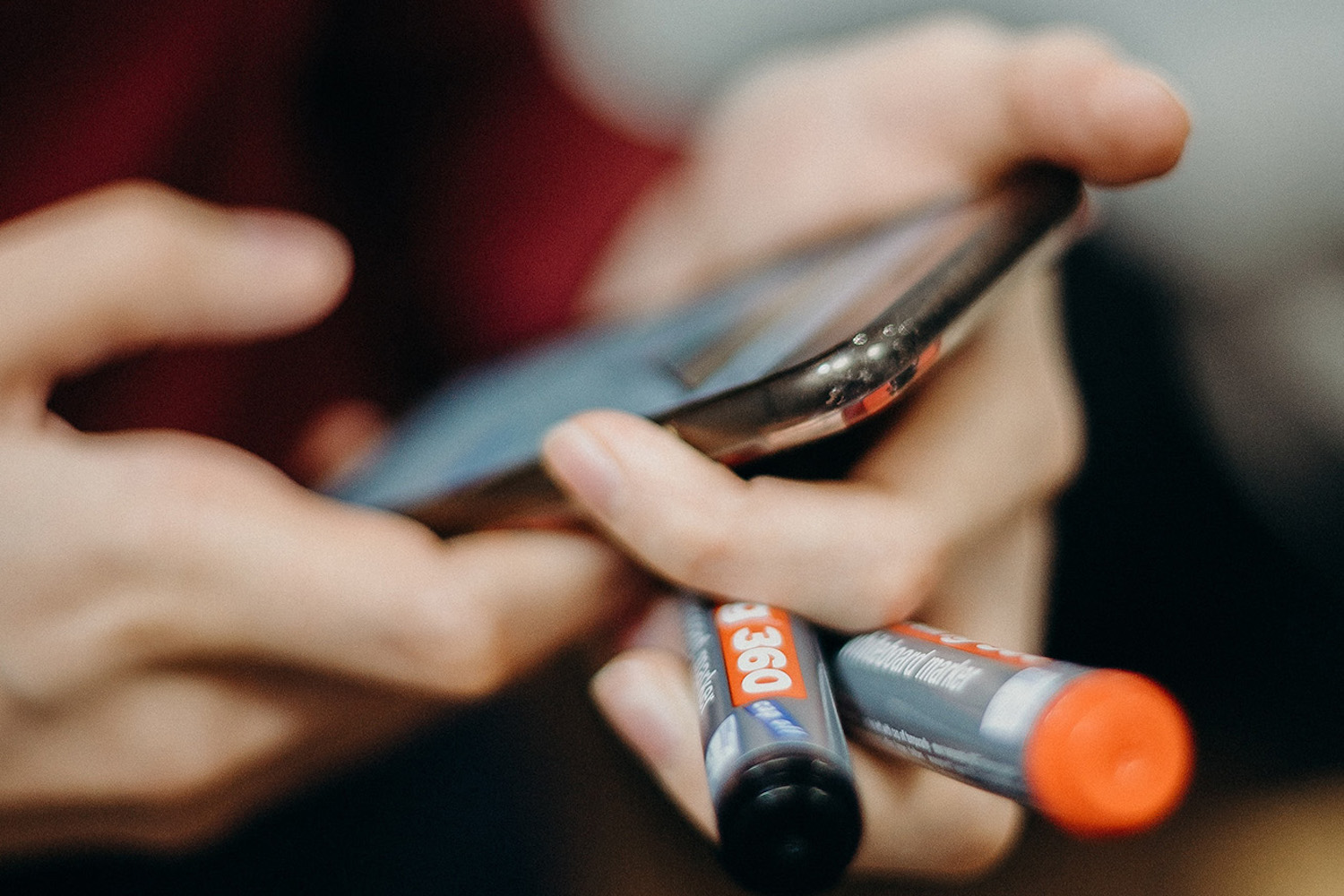 A person holding a mobile phone and two marker pens